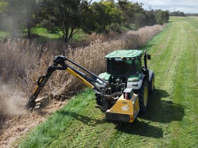 A reach mower cutting vegetation in a drain 